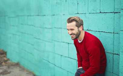 man wearing a red sweater leaning on a blue wall
